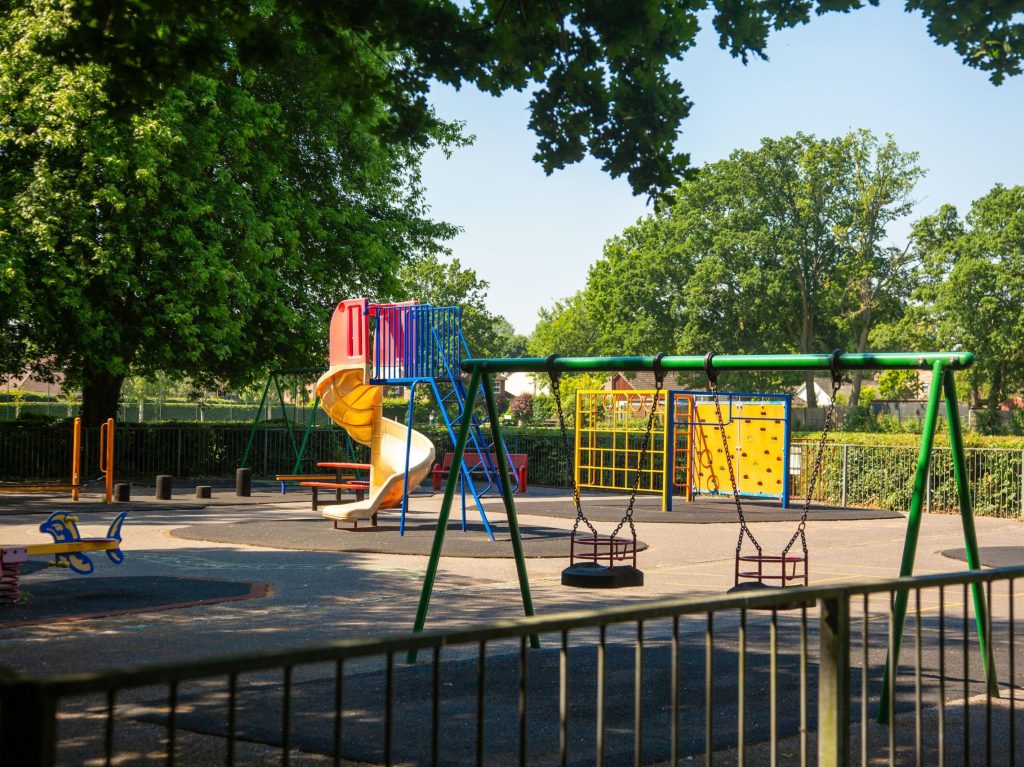 Image of brightly coloured swings, fun helter-skelter style slide and climbing frame at Oakley Park.