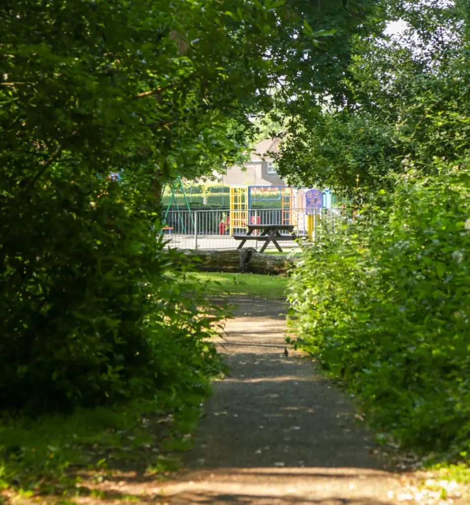 Image of a picnic bench and brightly coloured play equipment viewed from a distance between bushes