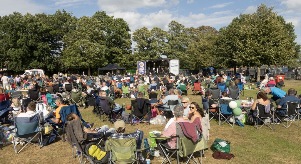 Image of the music on the views events - crowds sat on picnic chairs in the park in front of a stage