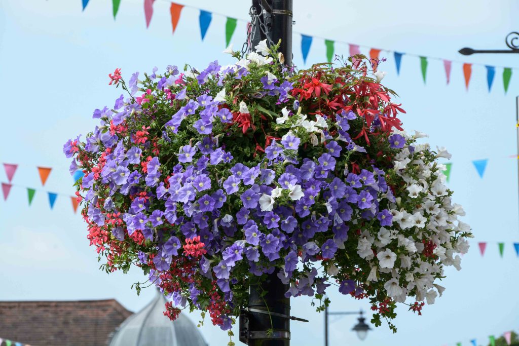 Image of a lamppost floral display of prupel and pink folowers with colourful bunting in the background