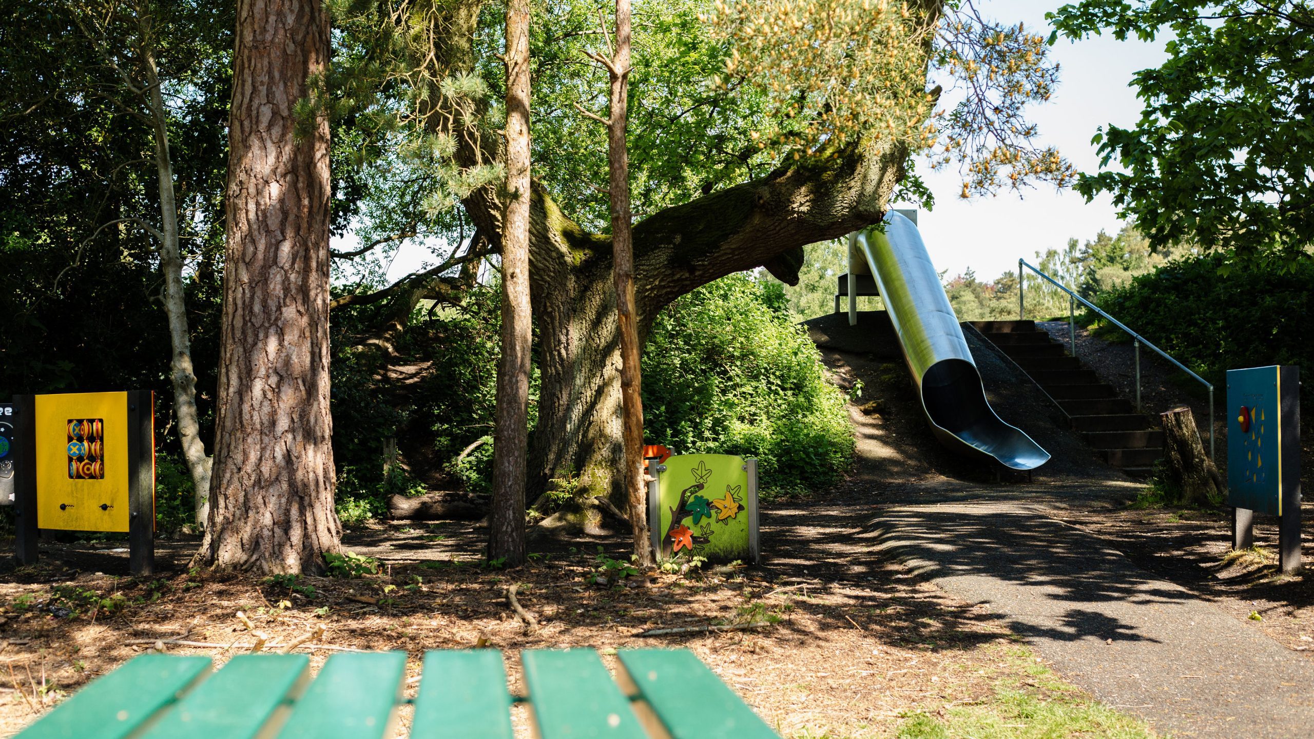Image of children's play area at calthorpe park showing woodland, metal tube slide and activity walls